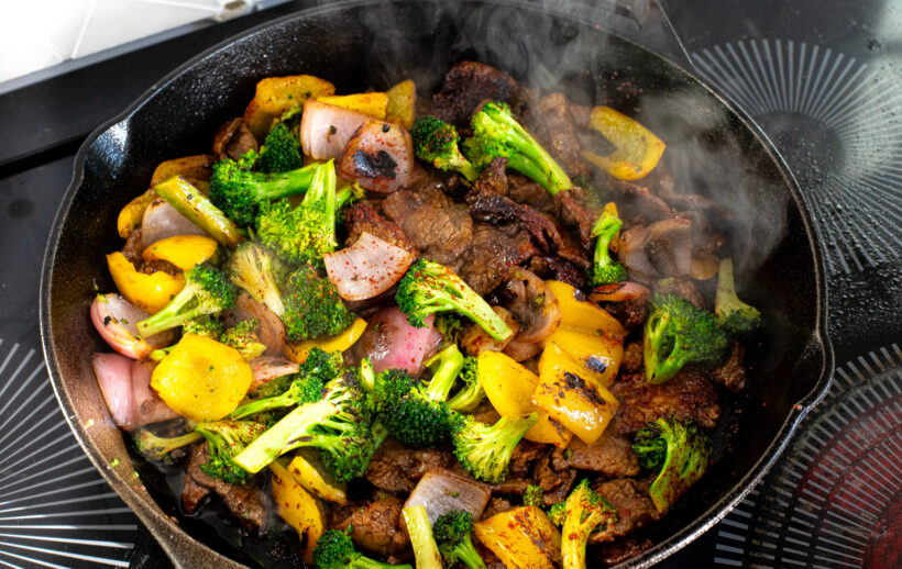 Stir fry vegetables and flank steak in a skillet.