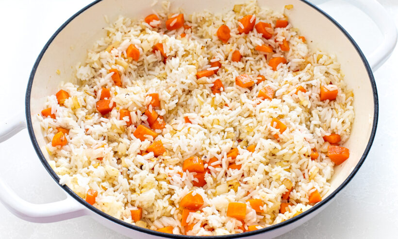 Rice with carrots and onions in a white sauté pan. 