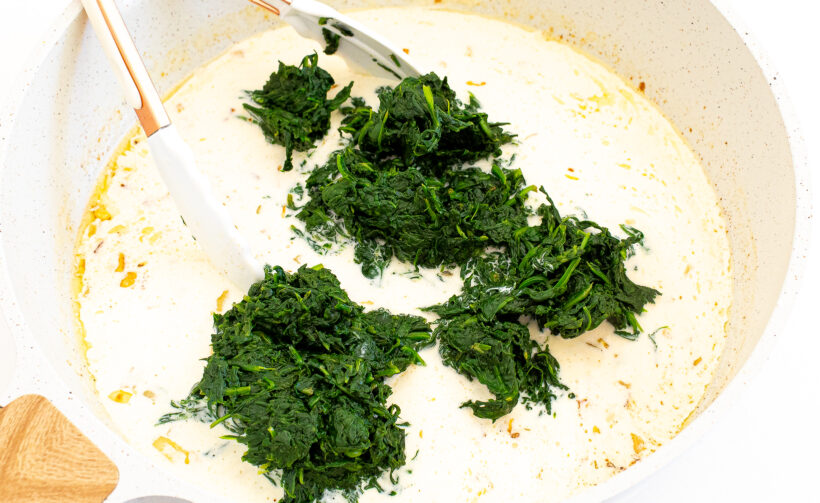 Heavy cream with onions and garlic in a skillet and spinach added. 