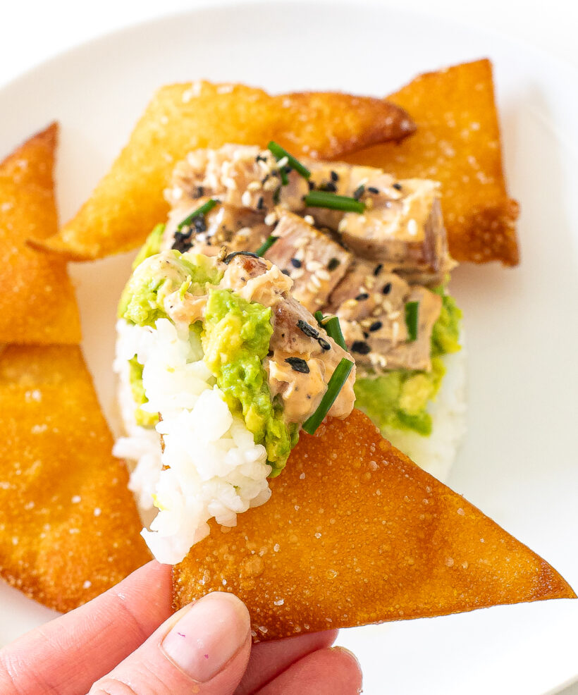 Hand holding a wonton chip that was dipped into the sushi stack.