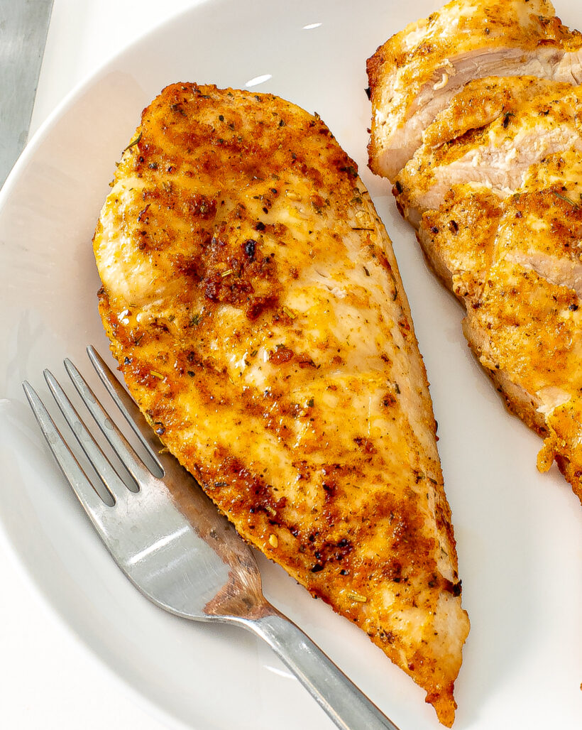 Chicken breast on a plate with some of it sliced off.