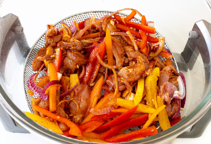Uncooked fajita ingredients in air fryer basket.