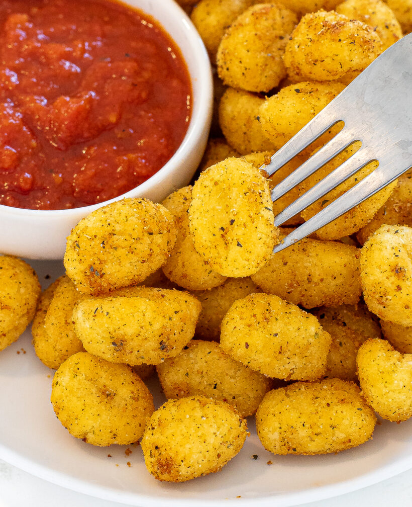 Air fried gnocchi on a plate with a fork picking one up to dip.