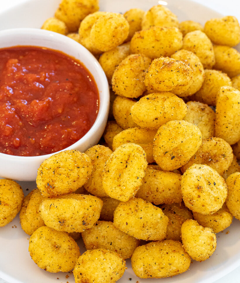 Air fryer gnocchi on a plate next to a small bowl of tomato sauce.