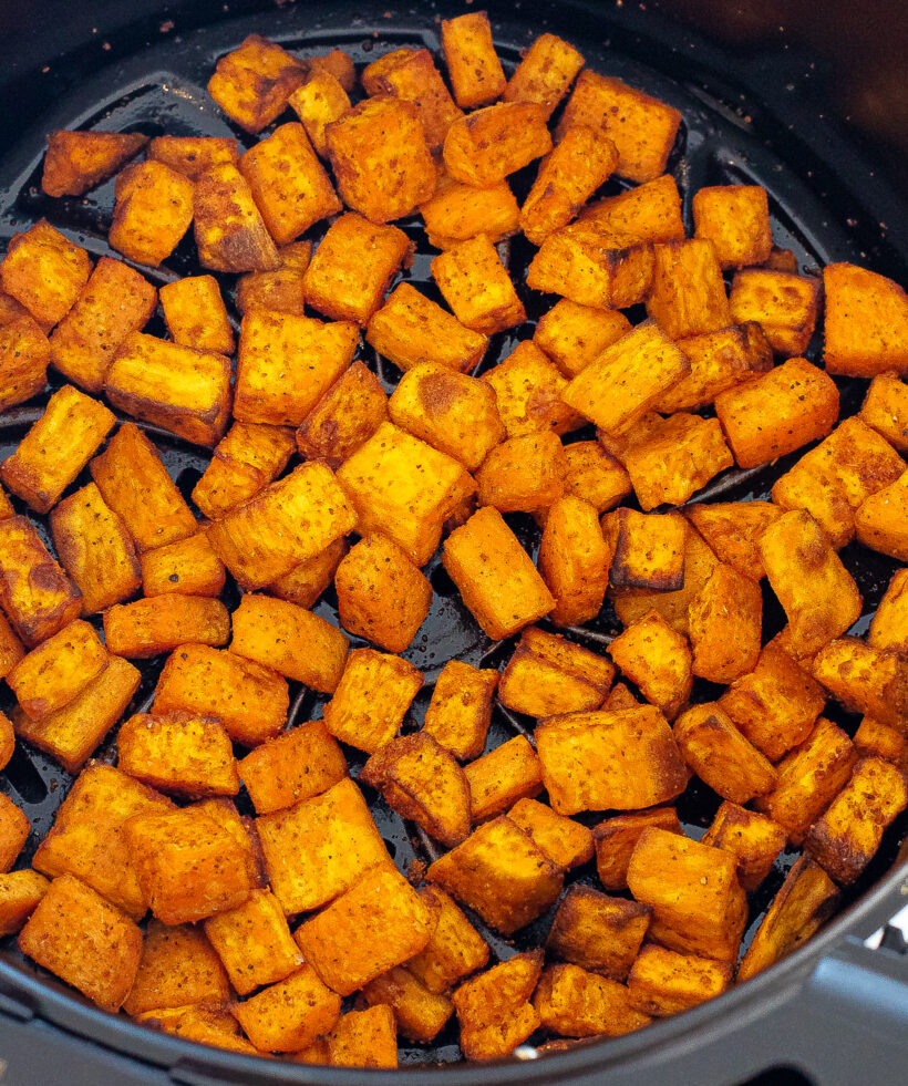 Diced sweet potatoes in an air fryer basket after being cooked.