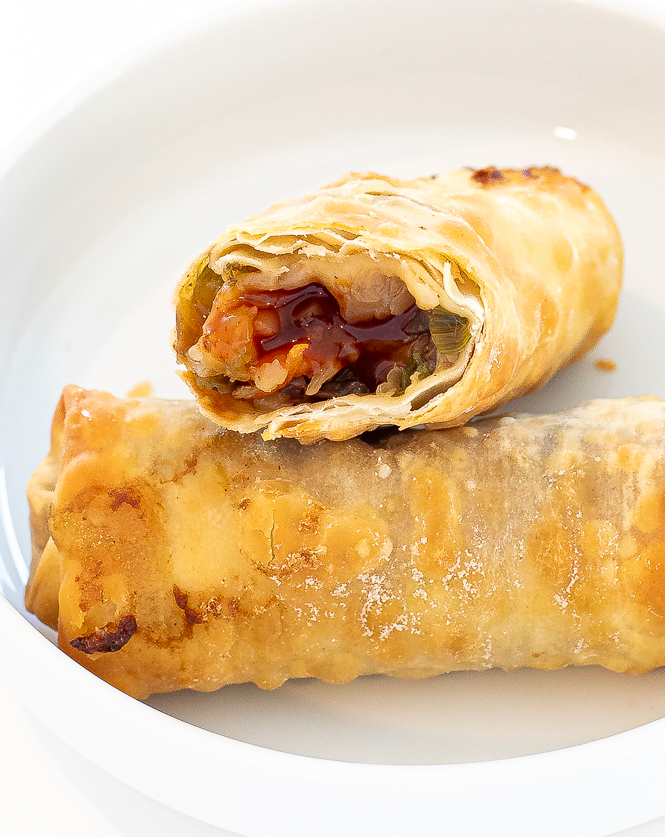 Egg roll broken in half to show the filling, stacked on another egg roll on a white plate. 