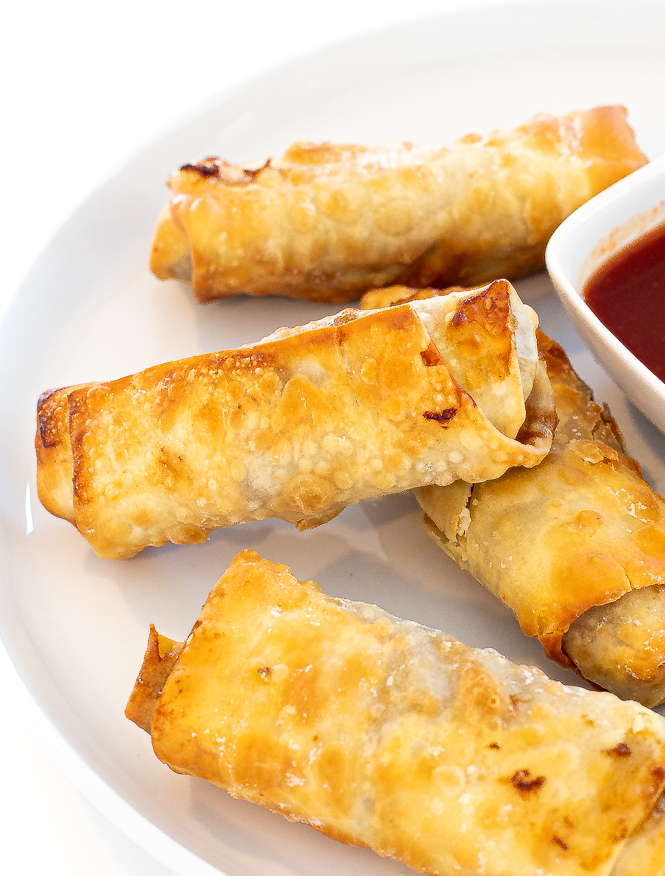Egg rolls stacked on a white plate. 