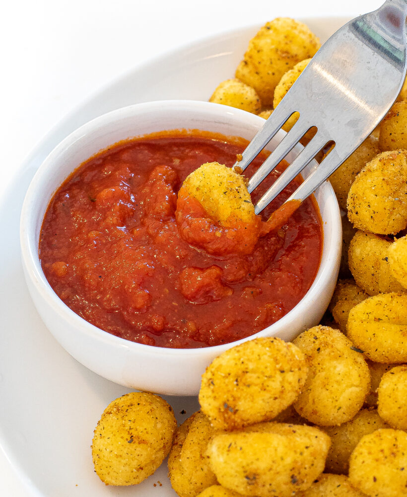 Fork with a gnocchi on it being dipped into tomato sauce.