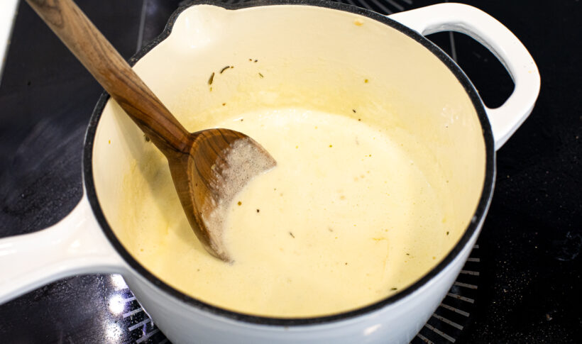 Alfredo sauce in a sauce pan with a wooden spoon.