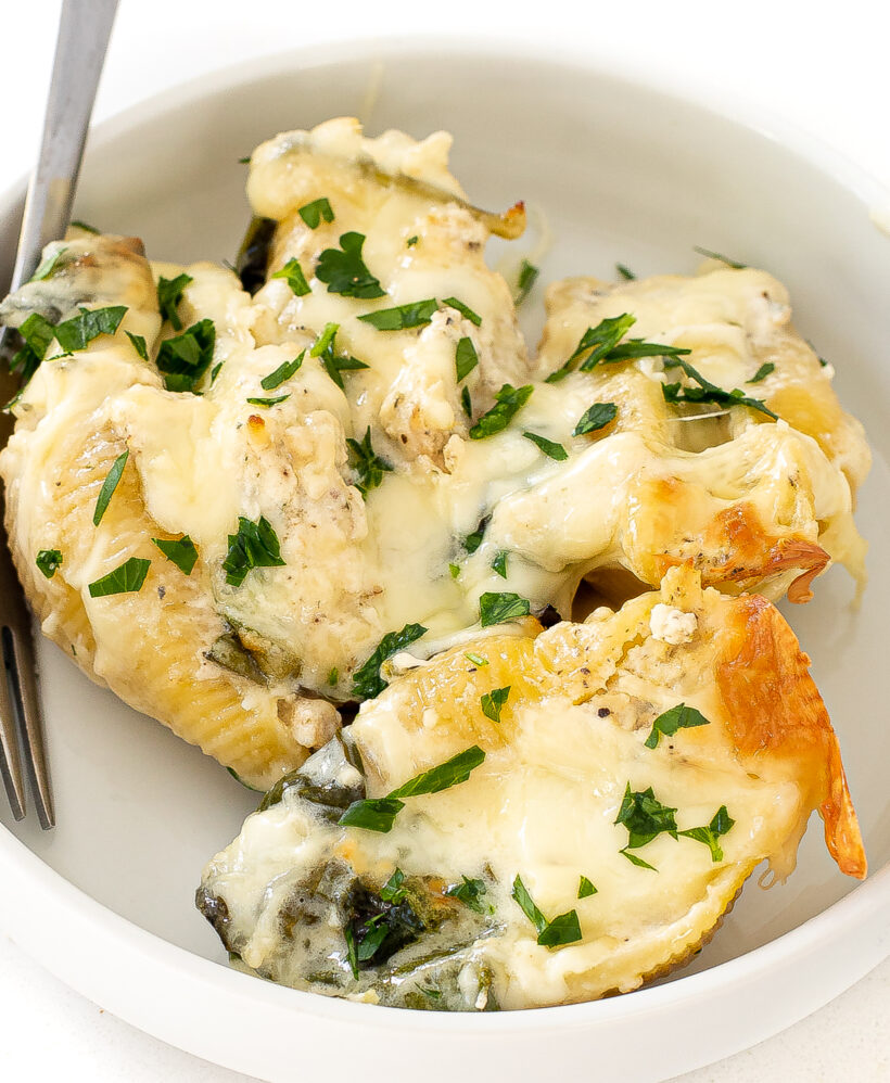 Close up shot of alfredo stuffed shells served in white dish. 