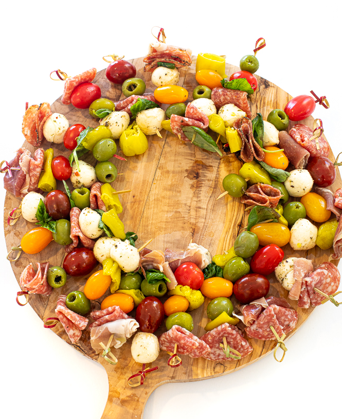 Skewers of antipasto arranged in a circle to replicate a wreath, on a wooden surface. 