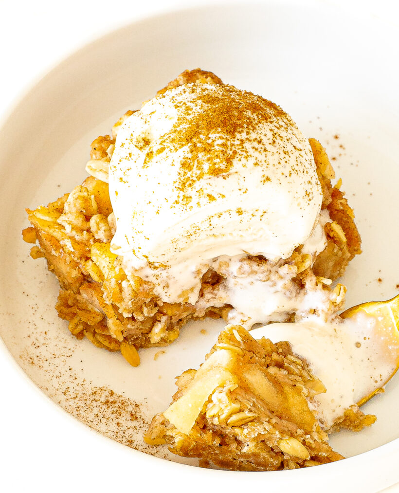 A slice of healthier apple crumb bars topped with ice cream on a white plate.