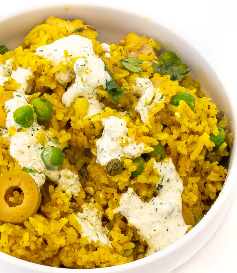 Arroz con pollo served in a white bowl with the sauce drizzled on top.