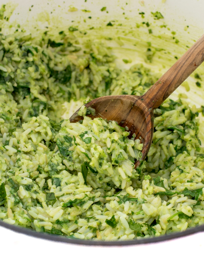Green rice in a white pot with a wooden spoon.