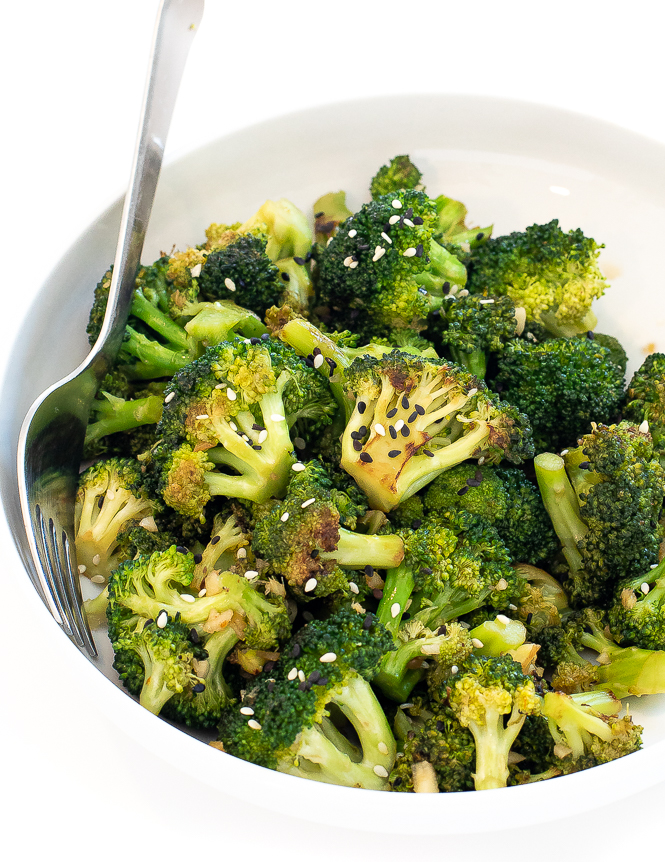 Broccoli in a white bowl with sesame seeds on top and a silver fork. 