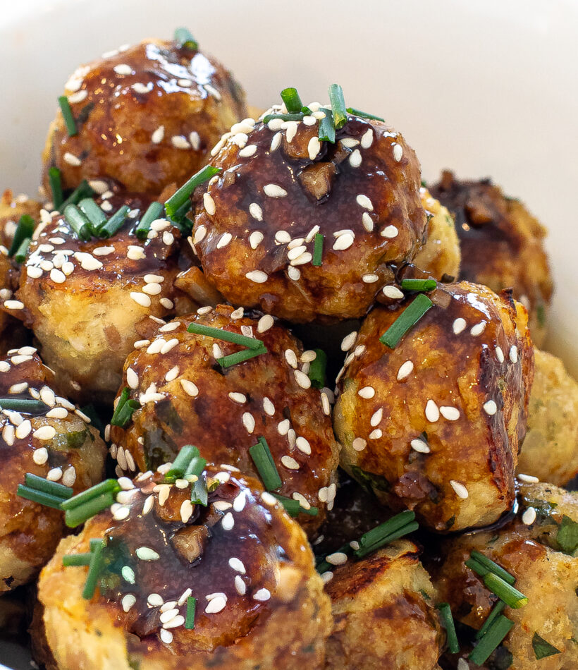 close up shot of asian chicken meatballs in white bowl with sesame seeds and green onions