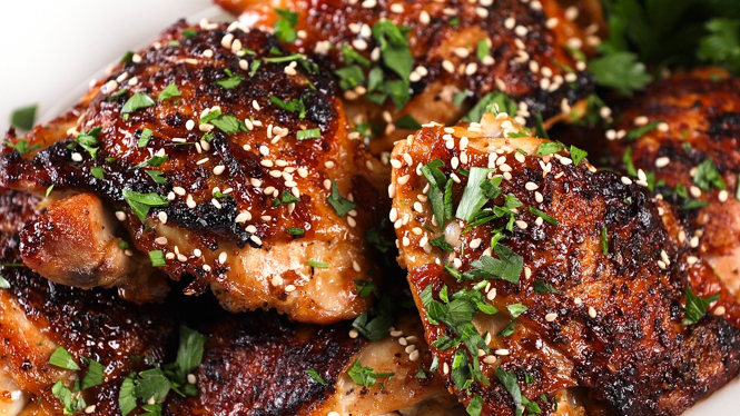 close up of Sticky Asian Chicken Thighs in a white dish, garnished with parsley and sesame seeds