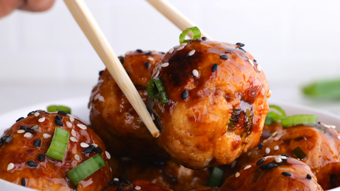 Chopsticks taking a meatball from a white bowl full of meatballs.