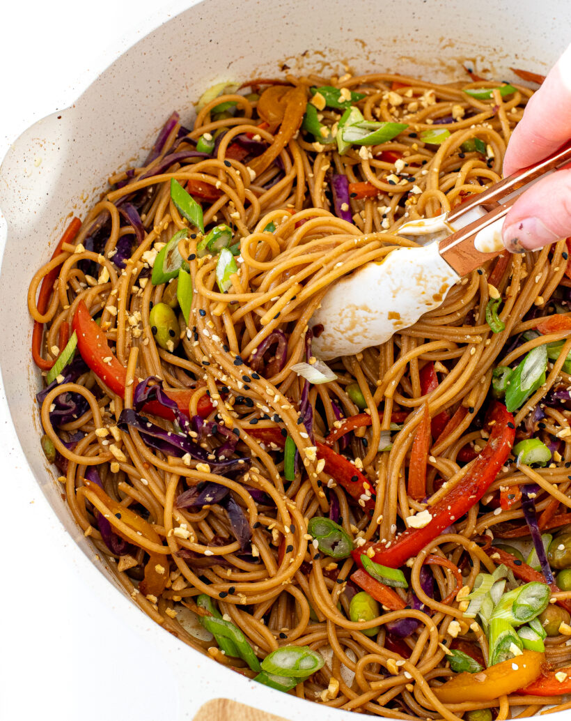 author scooping up rainbow stir fried noodles with tongs