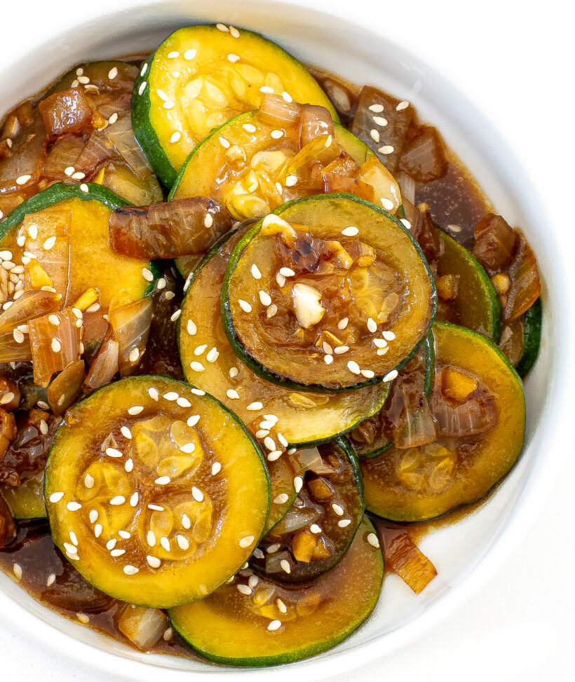A close up view of zucchini stir fry topped with sesame seeds in a white bowl.