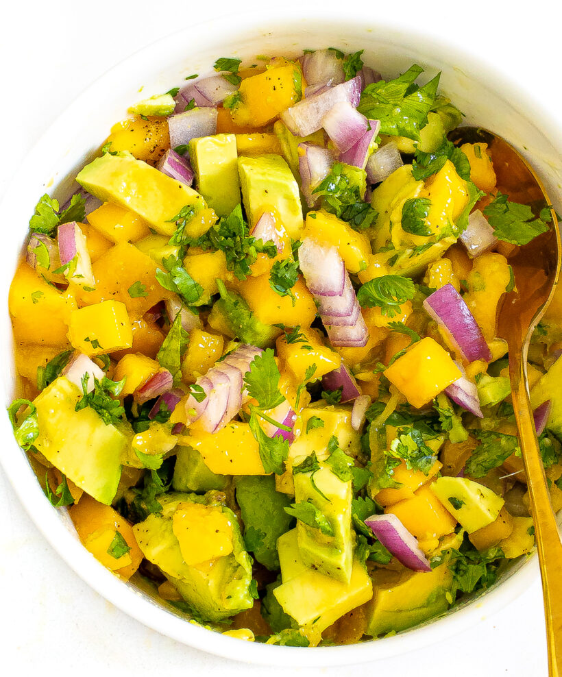 Mango avocado salsa served in a white bowl with a golden spoon.