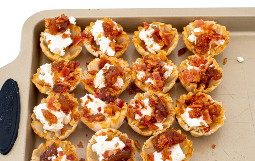 Phyllo cups filled with goat cheese, fig jam, and bacon on a baking sheet.