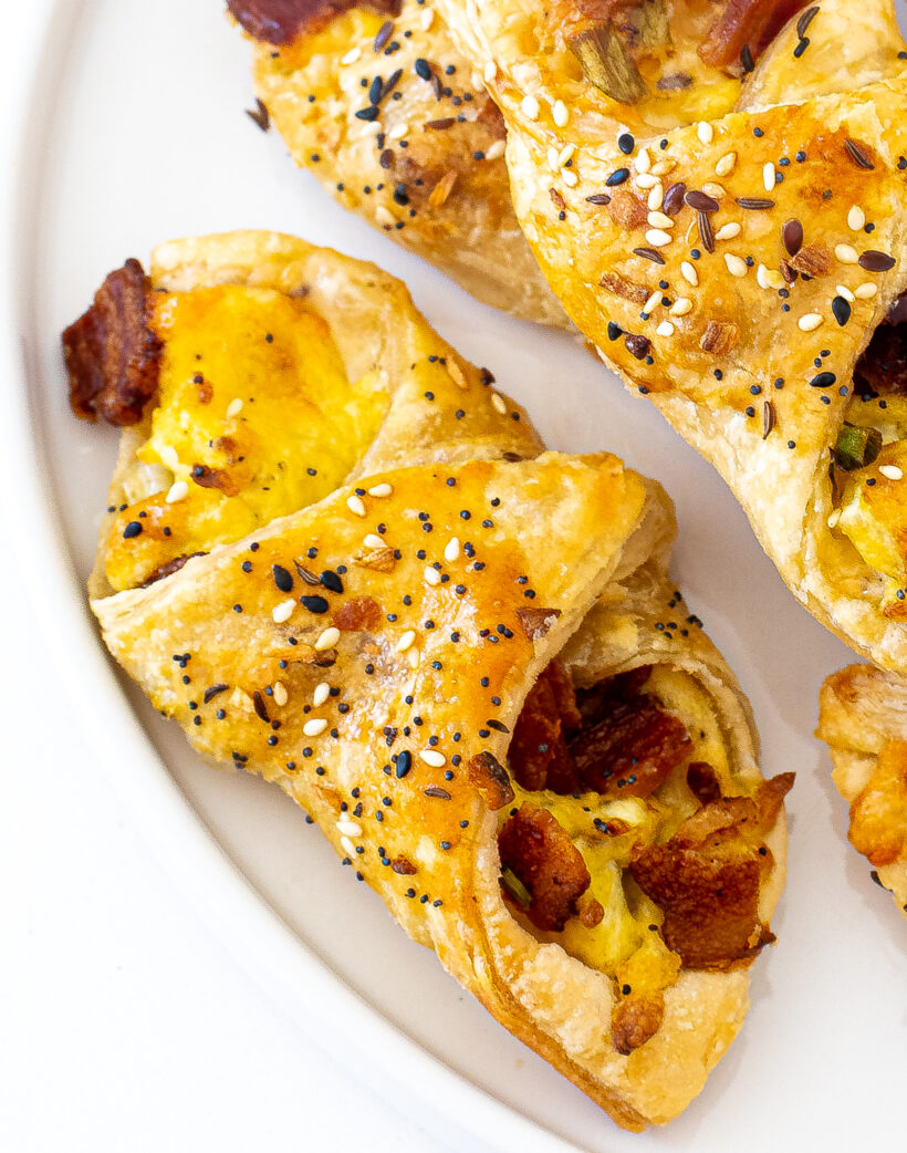 A close up photo of bacon egg and cheese pastries on a white plate.