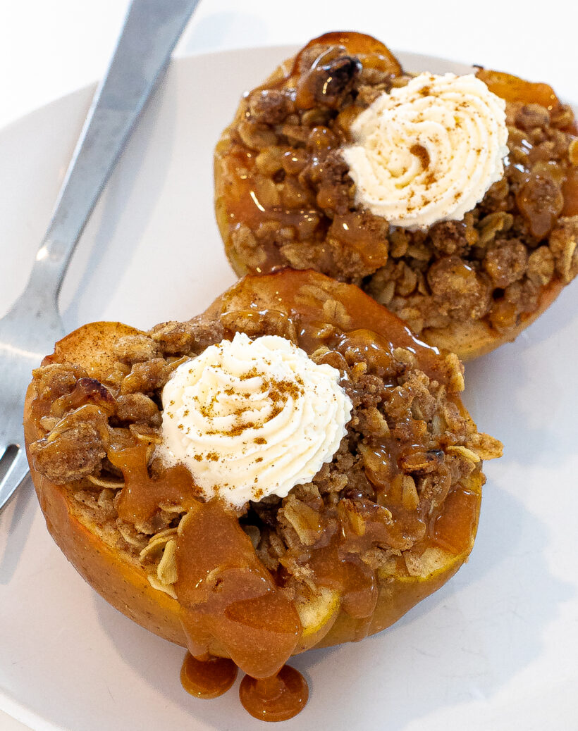 Two baked stuffed apples on a plate topped with whipped cream and caramel drizzle.
