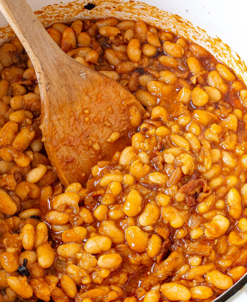 Overhead shot of baked beans in a Dutch oven pot with a wooden spoon.