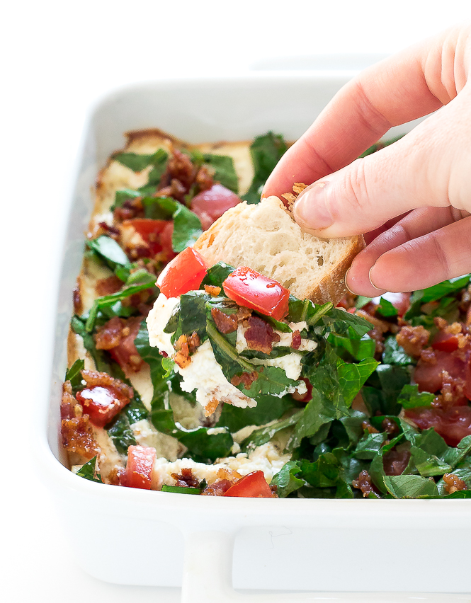 Baked BLT Dip | chefsavvy.com Hand dipping a piece of bread into the dip in a white baking dish.