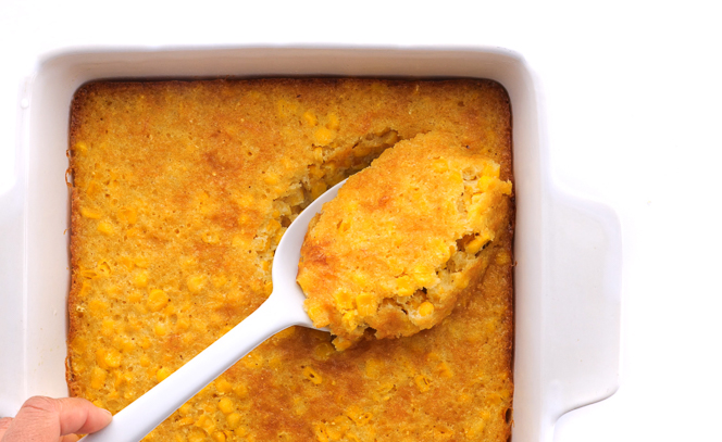 scooping corn casserole out of a baking dish