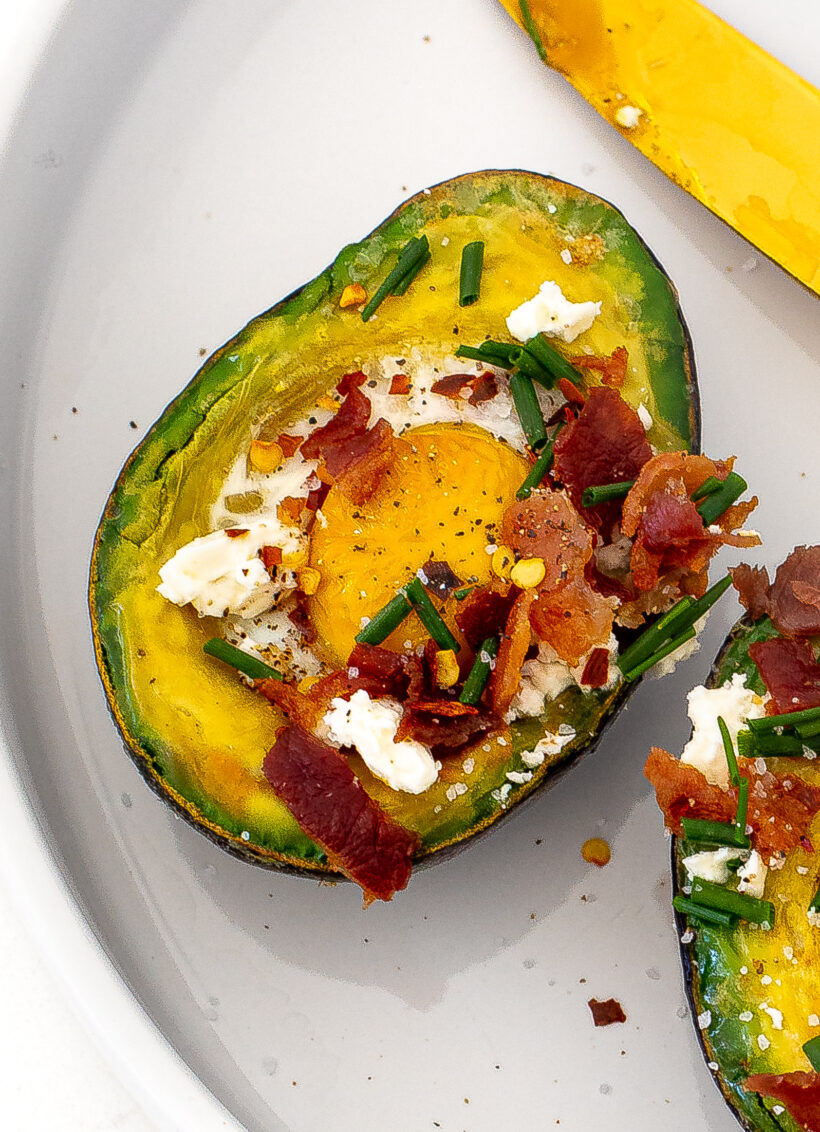 Close up shot of avocado with egg, bacon, chives and feta.
