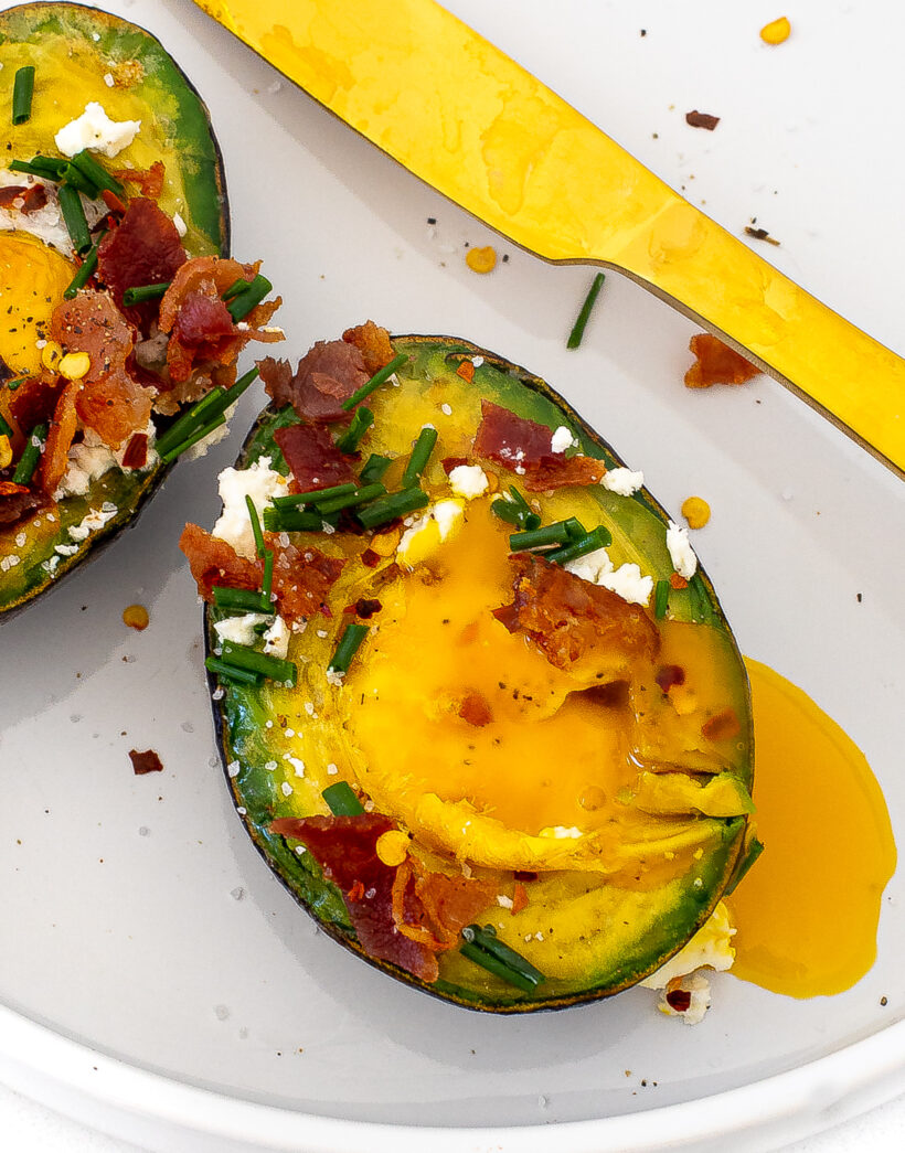 Baked eggs in avocado with the egg broken and running.