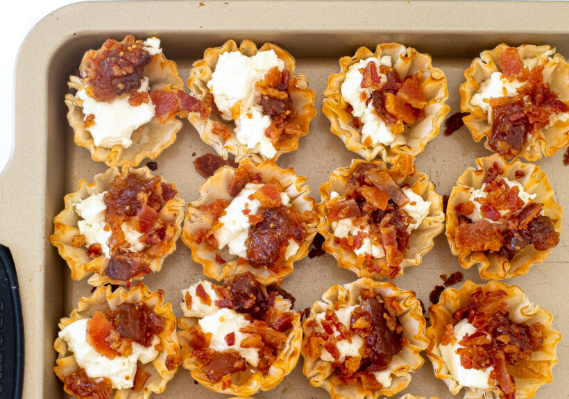 Phyllo cups filled with goat cheese, fig jam, and bacon on a baking sheet.