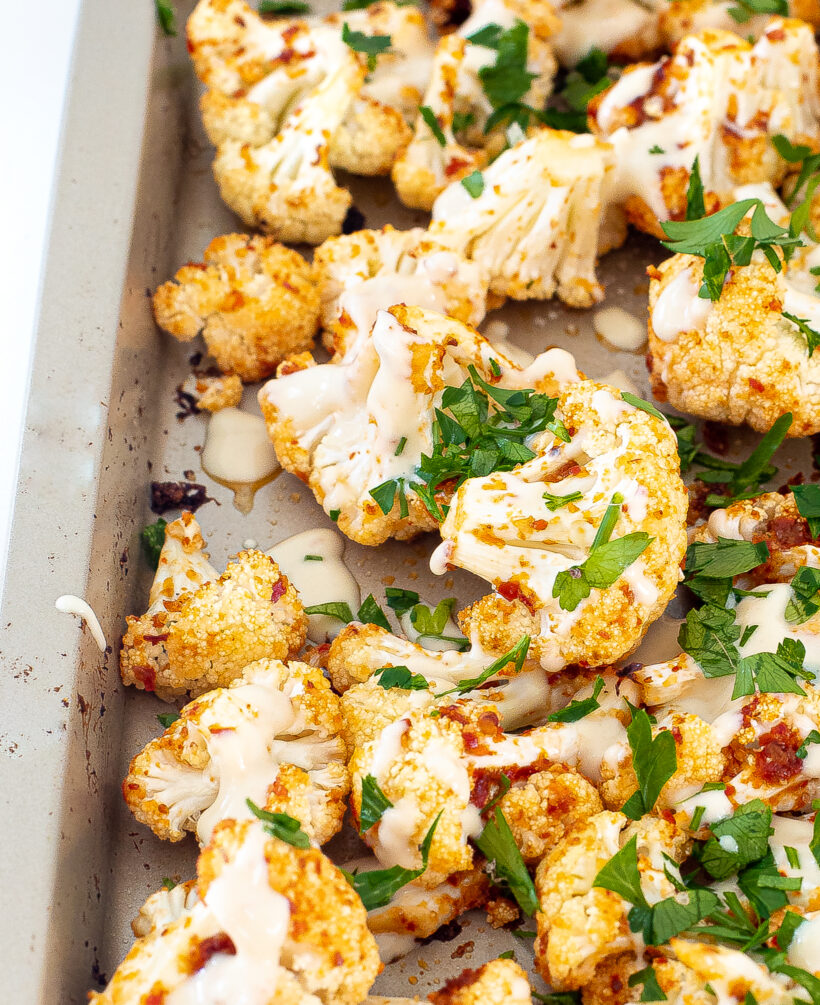 Cauliflower with harissa on the sheet pan after being drizzled with tahini sauce.