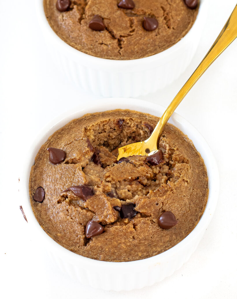 Baked oats in a white ramekin with a gold spoon taking a bite. 