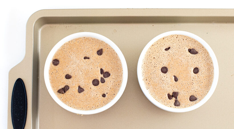 Baked oats batter in two ramekins with chocolate chips on top. 