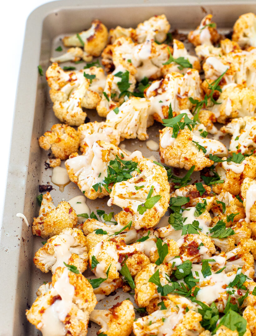 Cauliflower on a sheet pan after being roasted and drizzled with tahini sauce.