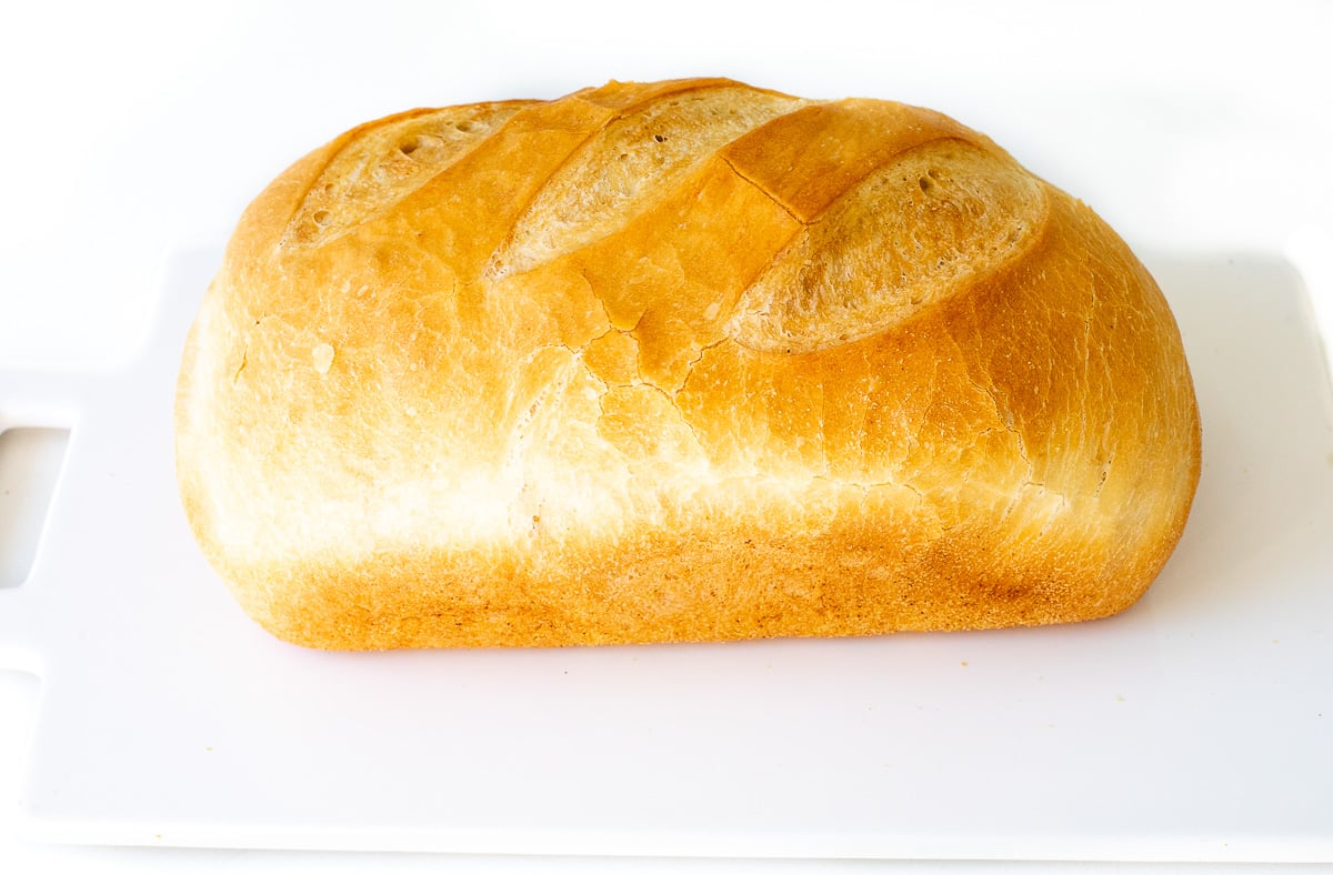 A golden-brown loaf of bread with scored crust on a white cutting board.