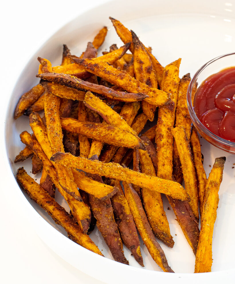 Crispy sweet potato fries on a plate with a side of ketchup.