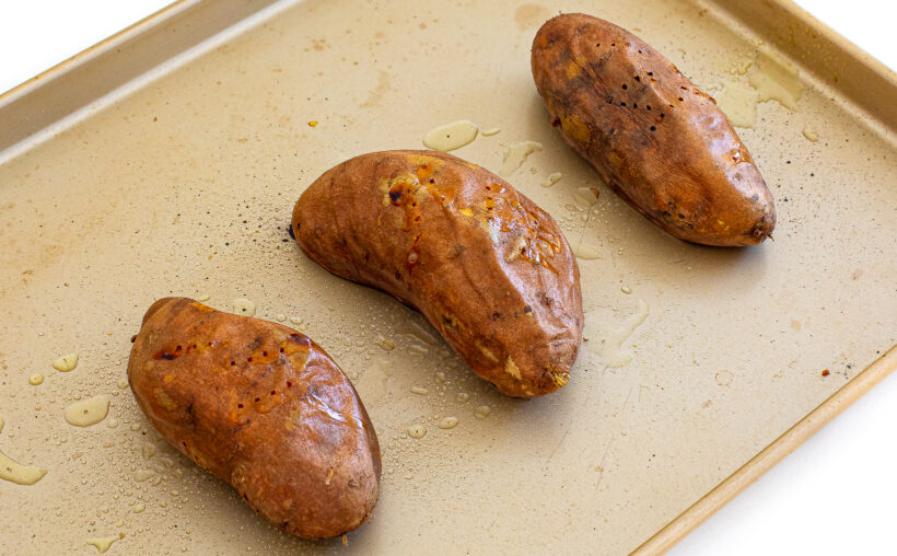 Three sweet potatoes on a sheet pan after being baked.