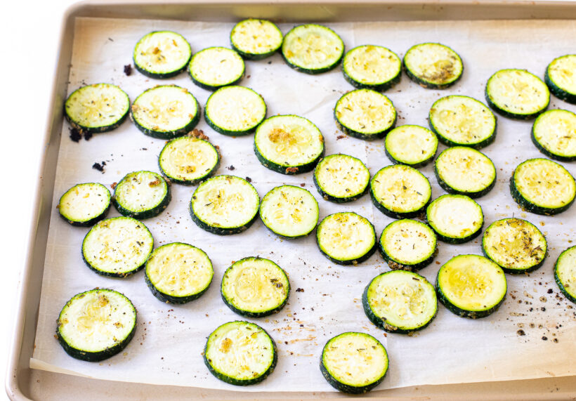 Zucchini slices on a baking sheet before being baked.