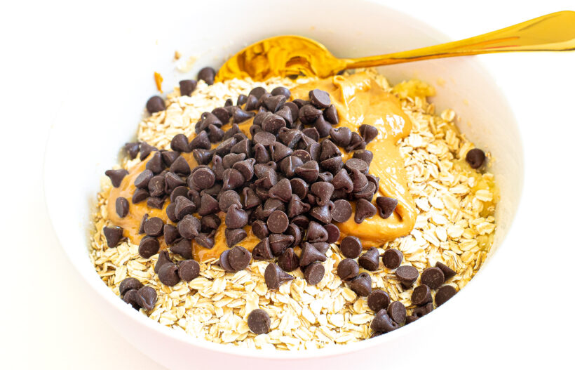 Oats, peanut butter, chocolate chips and mashed bananas in a mixing bowl.