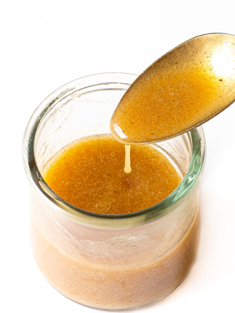 Banana bread syrup in a glass jar with a spoon drizzling some of the syrup.