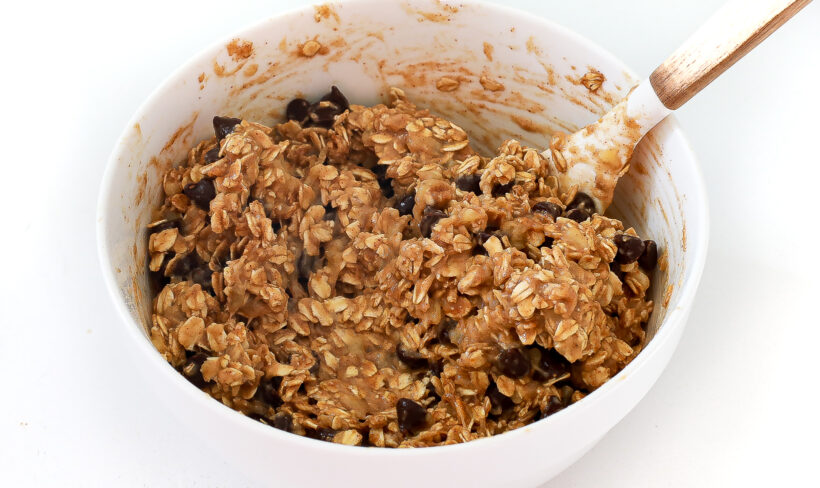Oatmeal mixture being mixed in a large white bowl with a rubber spatula. 