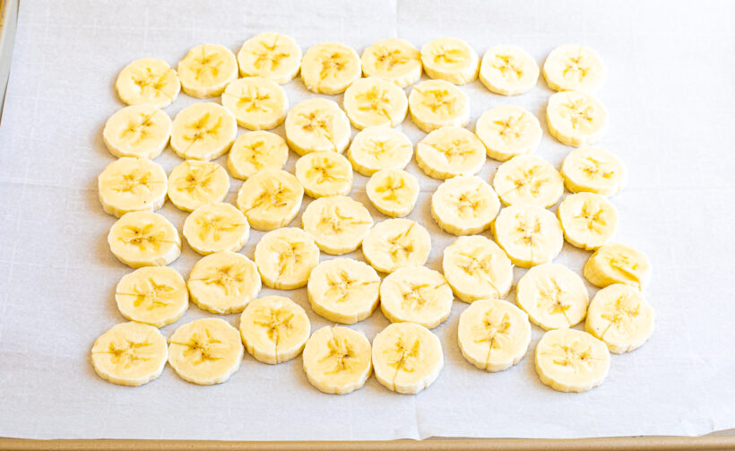 Banana slices lined up on a baking sheet lined with parchment paper. 