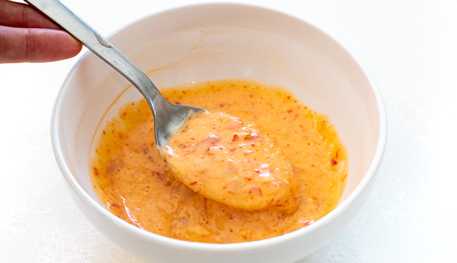 Bang bang sauce in a small white bowl with a silver spoon.