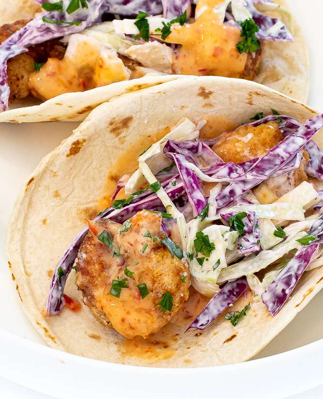 Shrimp tacos next to each other on a white plate. 