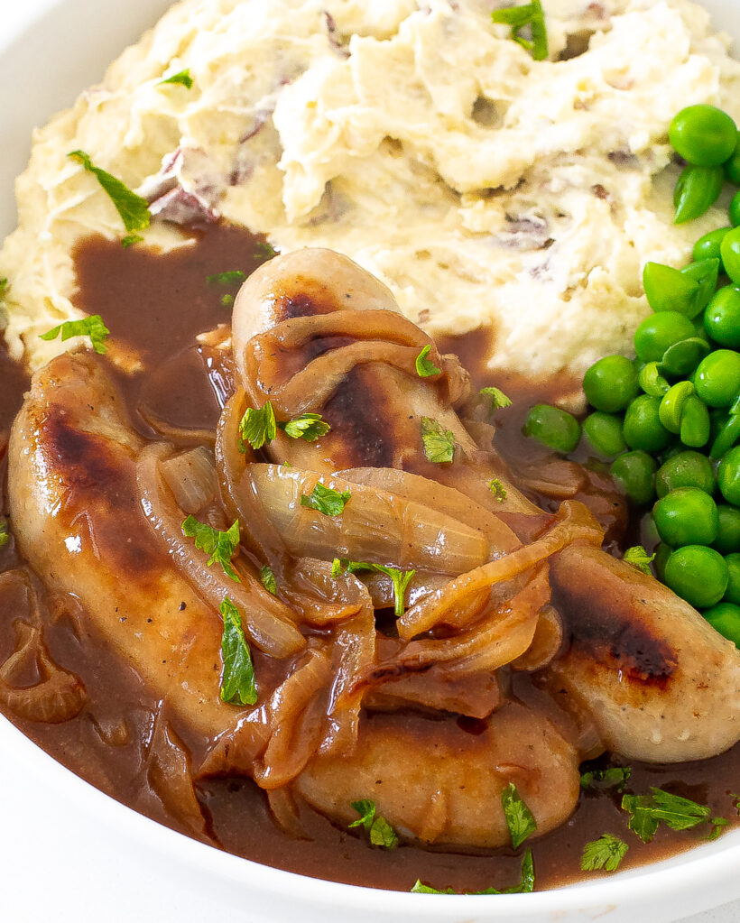 Two pork sausages with onion gravy, mashed potatoes and peas.