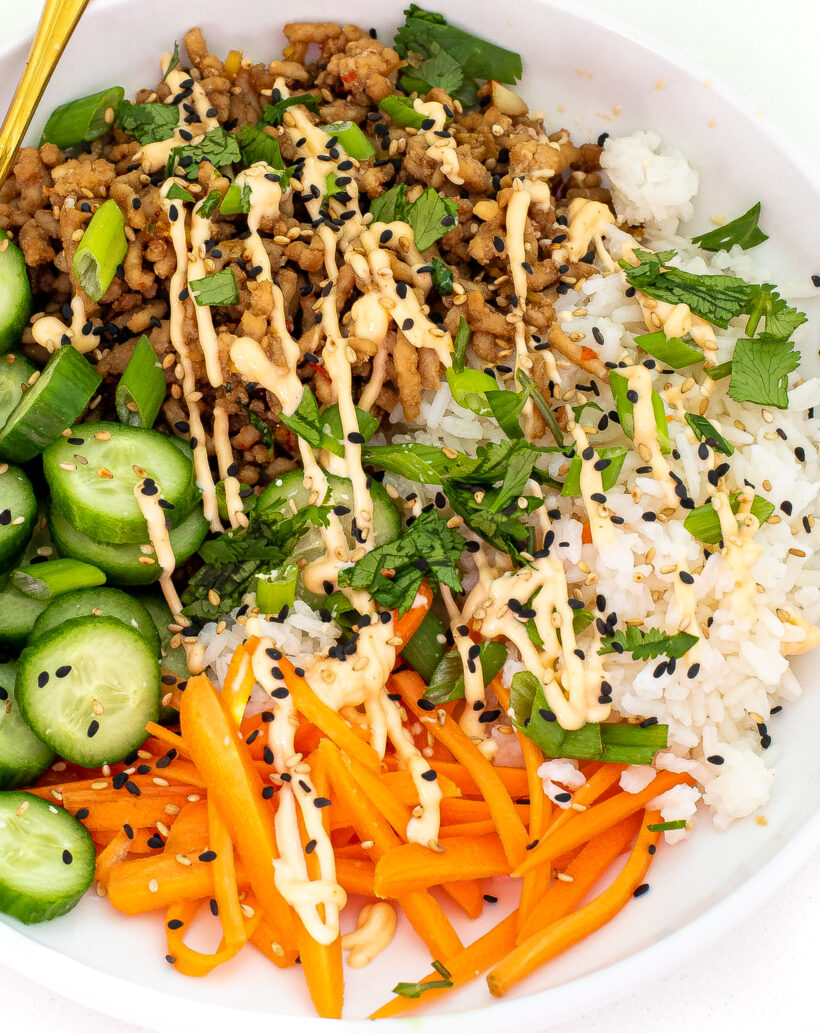 Banh mi bowl with chicken, rice, carrots, cucumbers and spicy mayo drizzled on top. 